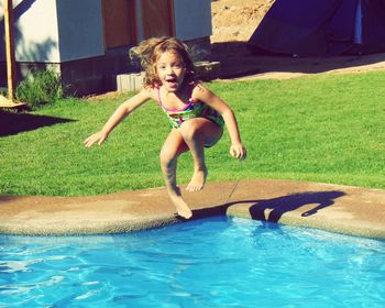 Happy girl jumping in swimming pool at yard