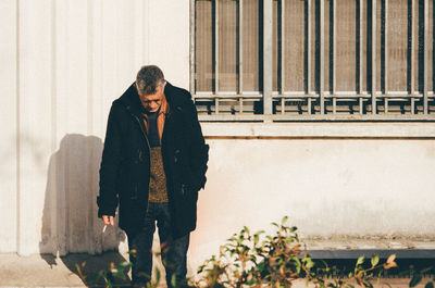 Senior man holding cigarette against building