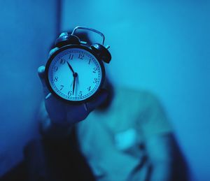 Man holding alarm clock while sitting against wall at home