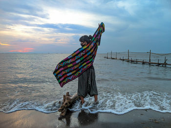 Woman with umbrella on beach against sky