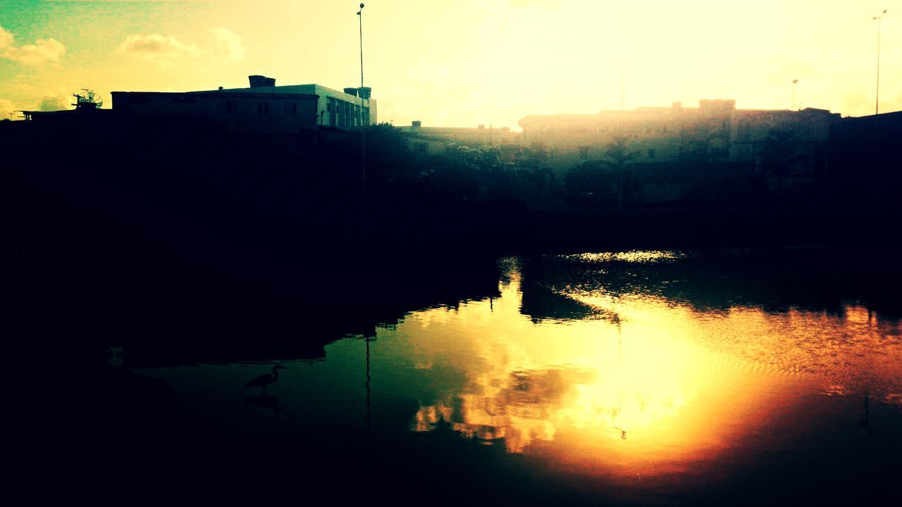 REFLECTION OF SILHOUETTE TREES IN WATER AGAINST SKY