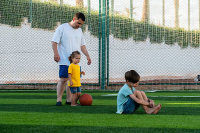 Sad boy sitting on green lawn and man with little girl standing behind and looking worriedly at him