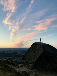 Silhouette man standing on rock against sky during sunset