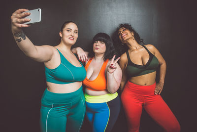 Smiling women taking selfie standing against wall