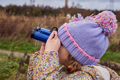 Rear view of woman holding hat on field