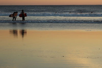 Silhouette surfers walking on the beach