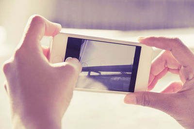 Close-up of hand photographing bridge through mobile phone