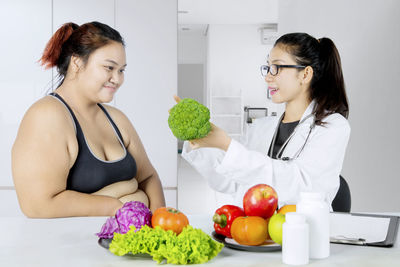 Dietitian showing vegetable to overweight patient at hospital