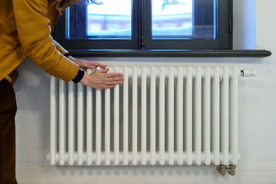 Woman warming hands near heating radiator after winter walk, female checking battery temperature