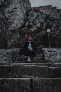 Low angle view of man sitting on steps against rock formations