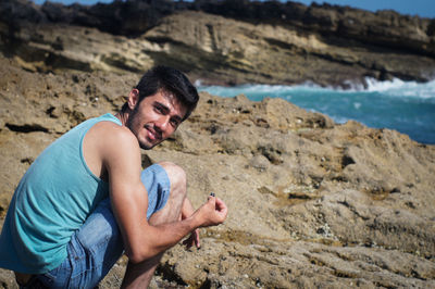 Portrait of smiling man crouching on shore at beach