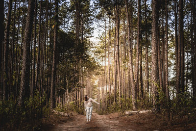 Woman standing on dirt road amidst trees in forest