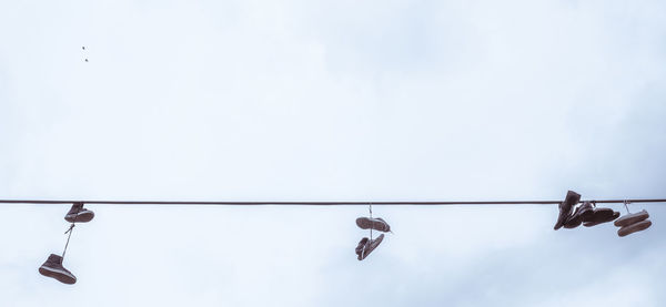 Low angle view of shoes hanging on cable against cloudy sky