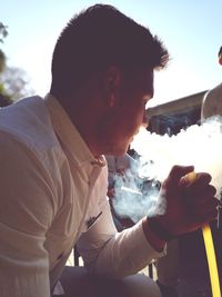 Side view of young man holding camera against sky