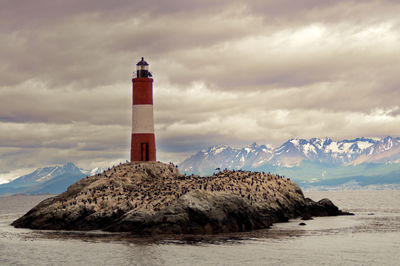 Lighthouse by sea and buildings against sky