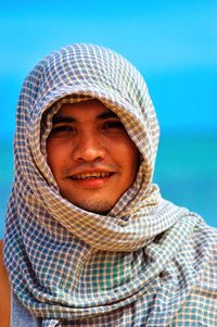 Portrait of smiling man wearing headscarf standing against blue sky