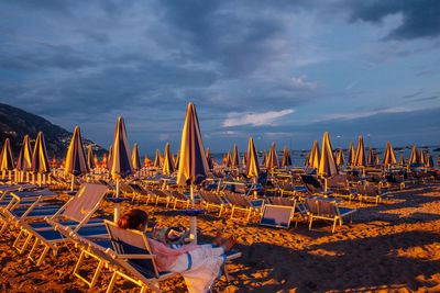 Man sitting on deck chairs at beach against sky