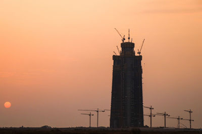 Silhouette of crane at construction site during sunset