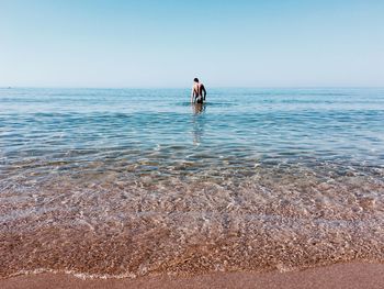 Rear view of woman standing on beach against clear sky