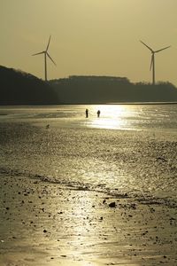 Silhouette of windmills by sea against sky during sunset