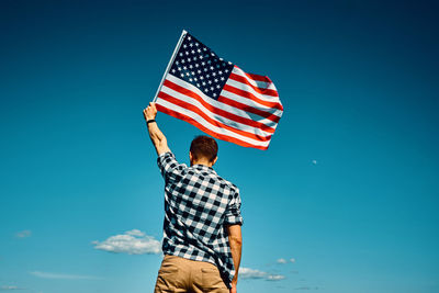 American flag outdoors. man holds usa national flag against blue cloudy sky. 4th july