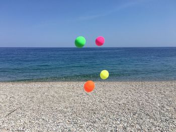 Multi colored balloons on beach against blue sky