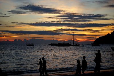 Silhouette people walking at beach against sky during sunset