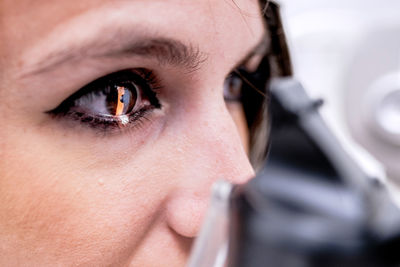 Closeup female patient with eye illuminated with light waiting for tonometer to finish measure intraocular pressure during eye examination in clinic