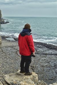 Rear view of boy standing on sea shore against sky