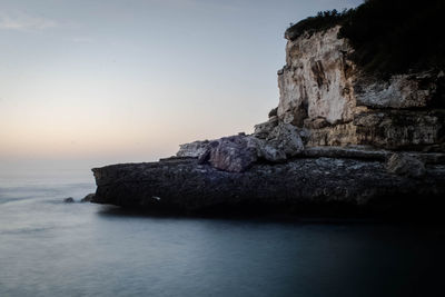 Rock formation in sea against sky during sunset