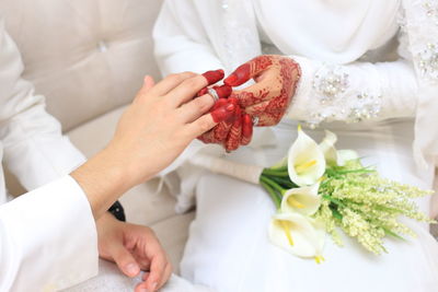 Midsection of bride putting ring in groom finger sitting on sofa during wedding