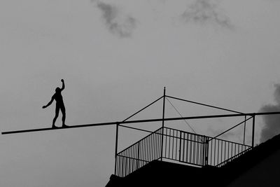 Low angle view of silhouette man walking on tightrope against sky during sunset