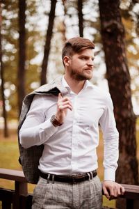 Young man looking away while standing by railing against trees in forest