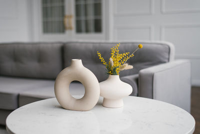 Modern ceramic vases with bouquets of mimosa flowers on a coffee table in the living room