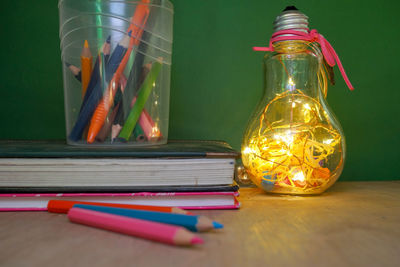 Close-up of illuminated light bulb by school supplies on table