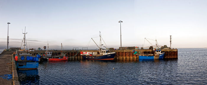 Fishing boats moored at harbor against clear sky