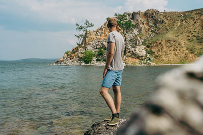 Full length of woman standing on rock by sea against sky