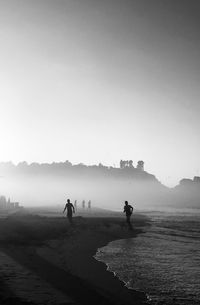 Silhouette people at beach against clear sky