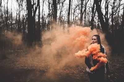 Young woman holding distress flare while standing in forest during winter