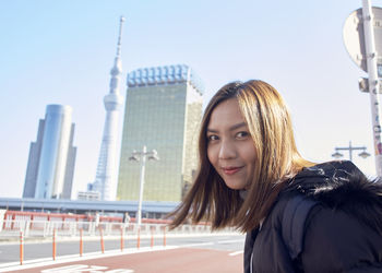 Portrait of beautiful woman in city against sky