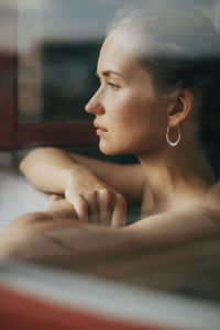 Portrait of woman looking away while sitting on window