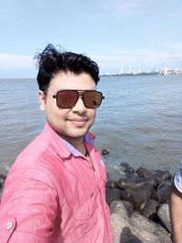 Portrait of young man wearing sunglasses at beach against sky