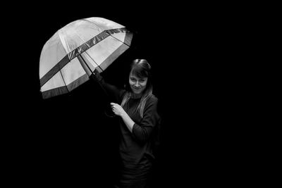 Portrait of woman with umbrella standing against black background