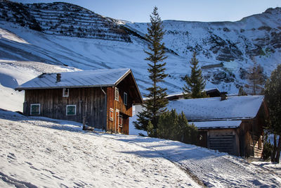 Snow covered houses by trees and mountains against sky