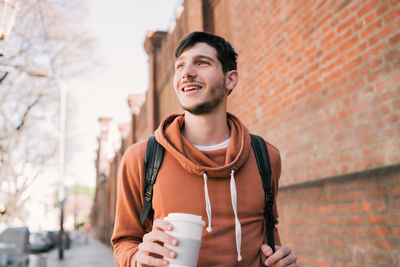 Young man holding coffee cup against wall