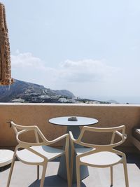 Empty chairs and table on beach against sky