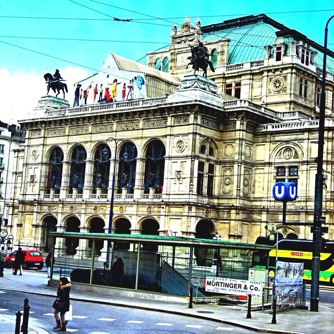 building exterior, architecture, built structure, street, city, text, human representation, transportation, walking, men, day, city life, road, incidental people, sky, outdoors, western script, facade