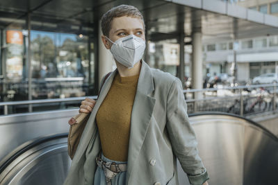 Woman wearing protective face mask looking away climbing on escalator in city
