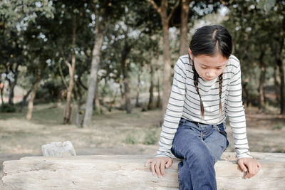 Girl sitting on bench against trees at park