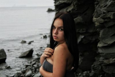 Portrait of young woman standing by rock formation at beach
